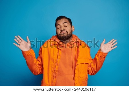 charismatic african american man in orange outfit showing that knows nothing on blue background