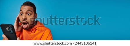 banner of surprised african american man scrolling social media in smartphone on blue background