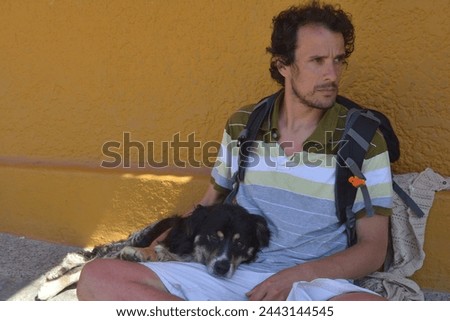 dark-haired young adult between 30 and 40 years old sitting with a dog with yellow wall in the background