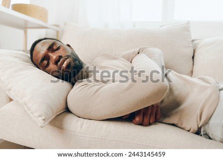 Stressed African American man suffering from a headache while sitting alone on a couch at home He appears tired, sick, and overwhelmed, displaying signs of anxiety and depression The room is an