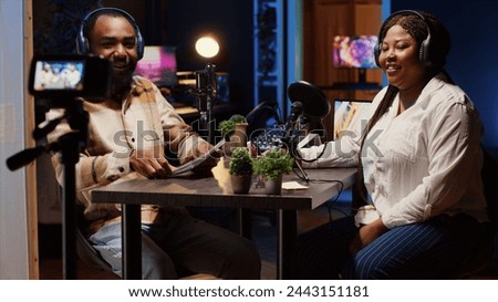 Vlogger show host and guest arriving in neon lights ornate personal studio, putting on headphones. Man and woman entering room, starting online podcast episode, greeting audience