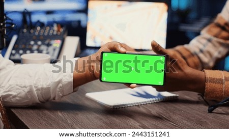 Man invited to podcast watching internet clips on green screen phone with host in apartment studio. Guest reacting to videos on mockup smartphone during online comedy show