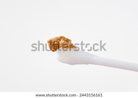 Ear wax plug isolated on white background. Removed giant ear wax plug on cotton swab closeup. Wax, which is also called cerumen on swab, macro shot. Cotton swab and ear hygiene. Remove earwax buildup Royalty-Free Stock Photo #2443156161