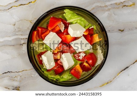 A bowl of salad with tomatoes, lettuce, and cheese. The salad is served on a marble countertop