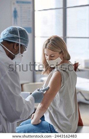 Vertical portrait of mature woman getting vaccine injection in clinic and wearing mask