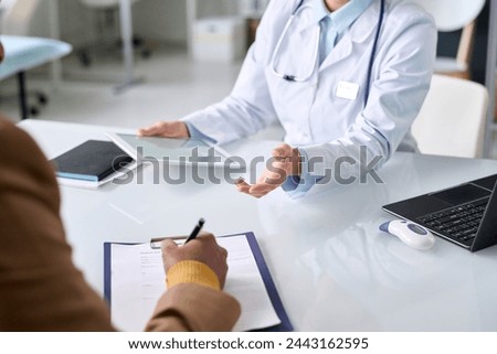 Close up of unrecognizable Middle Eastern man signing patients card on clipboard during consultation in medical clinic copy space