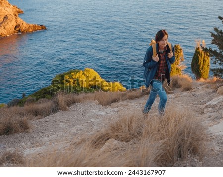 Young woman hiking on rocky beach in Spain, Benidorm. Watching the choppy sea and the bay. traveler enjoying freedom in serene nature landscape Royalty-Free Stock Photo #2443167907