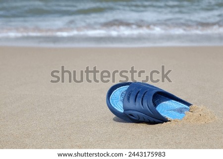One blue rubber slate slipper on a deserted sandy beach. Forgotten and lost things.