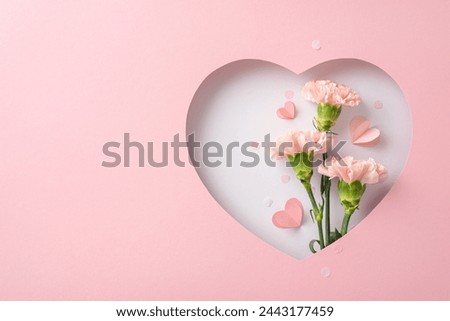 Mother's Day serenity concept. Top view of fragrant carnations, heartfelt cards, seen through heart silhouette on pastel pink backdrop, perfect for conveying love or advertising Mother's Day promotion Royalty-Free Stock Photo #2443177459