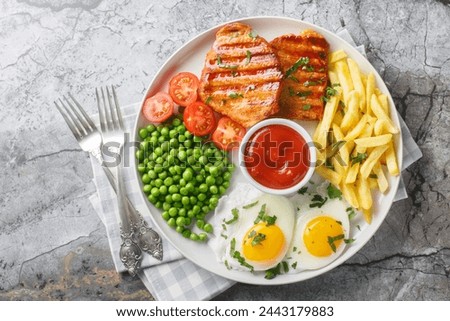 Tender grilled steak served with crisp golden French fries, fied eggs, green pea and fresh tomato closeup on the plate on the table. Horizontal top view from above
 Royalty-Free Stock Photo #2443179883
