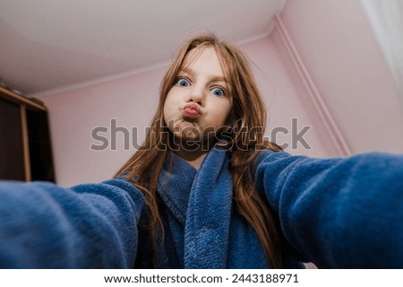 A smiling beautiful girl, a cheerful child teenager photographs herself with a camera, smartphone, phone showing a grimace on her face, smiling, grimacing. Photography, portrait.