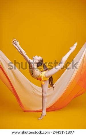 Gymnastics. Full-length portrait of a graceful young gymnast girl in a bright gymnastic leotard on a yellow studio background. Professional sports.