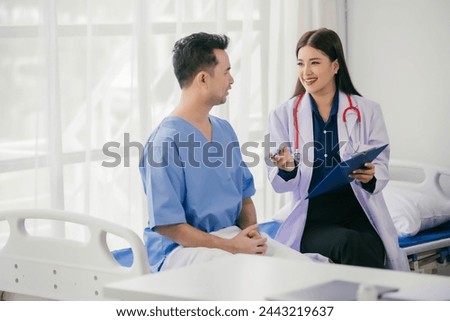 A woman in a white coat is talking to a man in a blue shirt. Scene is one of a doctor-patient interaction, with the doctor providing information Royalty-Free Stock Photo #2443219637