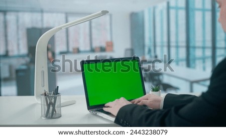 Businesswoman typing on a laptop keyboard with green screen in Office. Advertising area, workspace mock up.