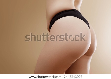 Back view of crop anonymous plump female in black panties with imperfect skin standing against beige background . Stretch marks on female legs. A woman's fat cellulite and a stretch mark