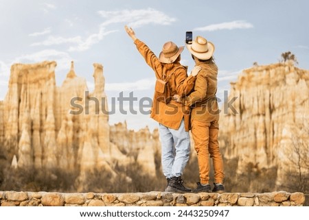 Two people are standing on a bridge, one of them taking a picture of the other. Scene is joyful and adventurous, as the two people are enjoying their time together in a beautiful natural setting