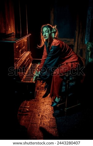 Halloween horrors. A scary clown girl, dressed in a red circus dress, looks at the camera, playing piano