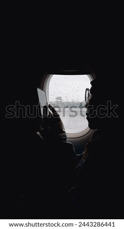 Asian woman in hijab sitting next to the window of a commercial airplane holding her smartphone, enjoying vacation by air transportation.