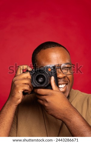 Black man smiling and holding camera to his face while taking a photo in the studio