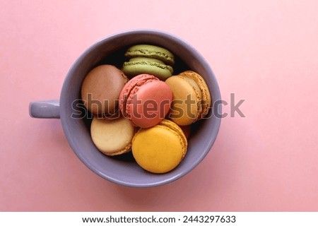 Purple cup filled with pastel macarons on pink background. Top view.