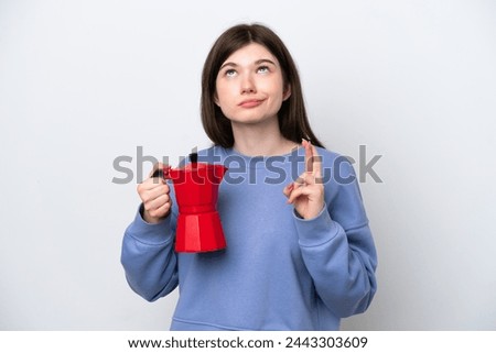 Young Russian woman holding coffee pot isolated on white background with fingers crossing and wishing the best