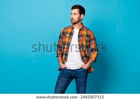 Photo of handsome cool man dressed plaid shirt hands in pockets look at business offer empty space isolated on blue color background