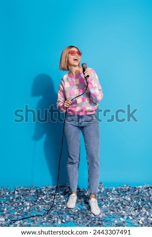 Vertical photo of pretty young girl sunglass celebrate party karaoke confetti wear trendy pink outfit isolated on blue color background