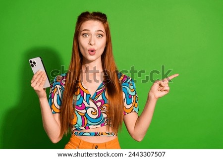 Photo portrait of attractive woman hold device shocked point empty space dressed stylish retro clothes isolated on green color background