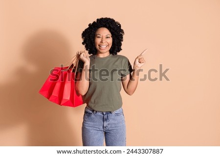 Photo of optimistic woman wear khaki t-shirt hold shopping bags indicating at offer empty space isolated on beige color background