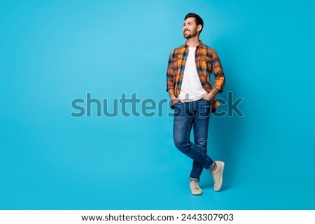 Full size photo of confident man dressed plaid shirt hold palms in pockets look at sale empty space isolated on blue color background