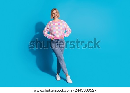 Full size photo of positive pretty woman dressed colorful sweater standing holding palms in pockets isolated on blue color background