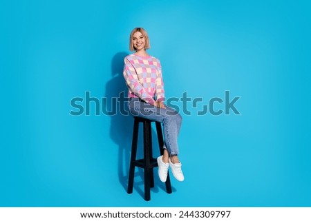 Full size photo of good mood gorgeous woman dressed colorful sweater denim pants sitting on bar stool isolated on blue color background
