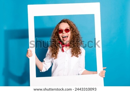 Photo portrait of nice young lady sunglass hold instant photo frame tongue out wear trendy white garment isolated on blue color background