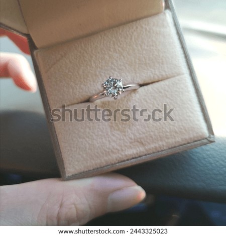 A hand holding a jewelry box of a 6-prong solitaire 1-carat diamond white gold engagement ring. Selective focus.  Royalty-Free Stock Photo #2443325023