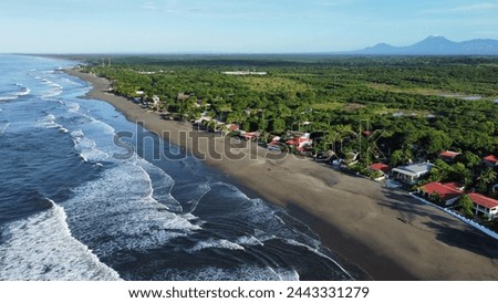 Aerial view of a beach at the pacific coast of Nicaragua with blue water, green forest and mountains in the background
