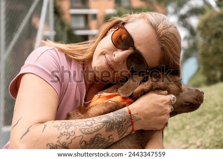 Close-up of a woman with closed eyes and sunglasses hugging her dog affectionately.
