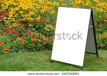 Mockup background of a blank A-frame signboard on a lush lawn with vibrant blooming flowers in a well-tended garden. Empty white board with copy space for your design.