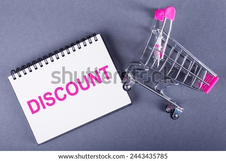 A shopping cart stands next to a notebook with the word discount written on it. The notebook appears to be related to business or financial activities, possibly suggesting a sale or promotional offer.