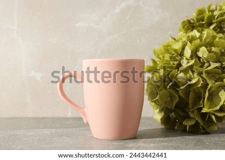 A pink cup with green hydrangeas in a vase