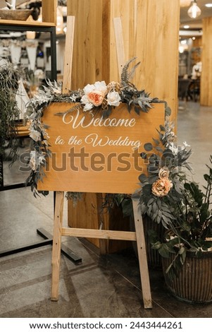 A wooden welcome sign covered in colorful flowers and lush greenery, creating a vibrant and inviting display. With the inscription "Welcome to the wedding"