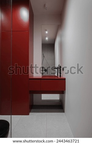 A bathroom featuring a red sink and black toilet fixture Royalty-Free Stock Photo #2443463721