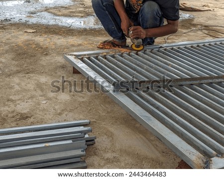A fence worker is smoothing an iron fence using a grinding machine, stock photo.