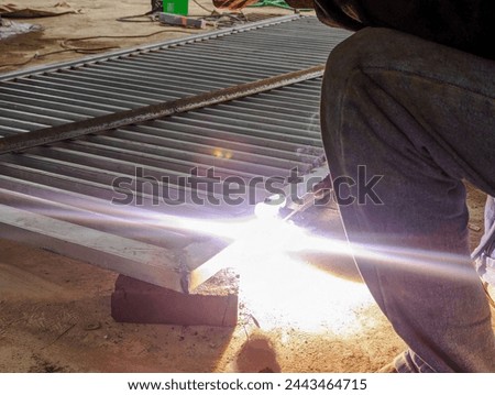 A fence worker is connecting a house with a fence using a welding machine, stock photo.