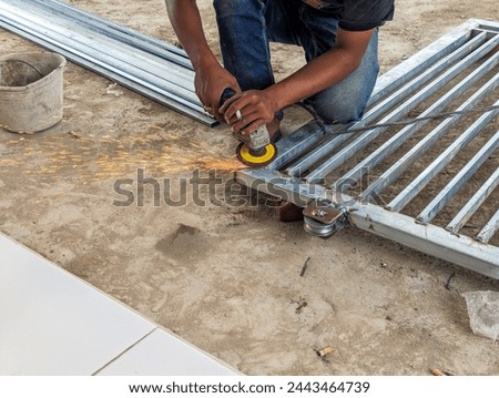 A fence worker is smoothing an iron fence using a grinding machine, stock photo. 