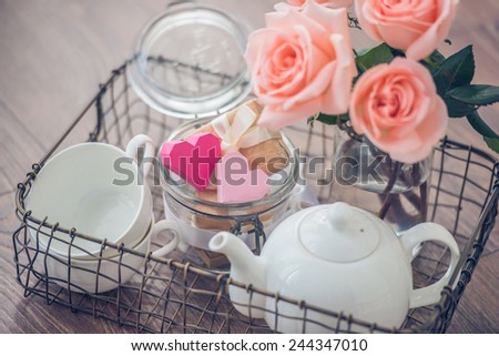 Tray with roses, white teapot, cups and valentine's paper hearts in retro jar. Toned picture