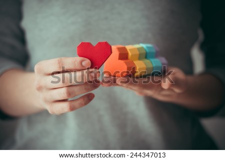Hands holding  rainbow paper hearts, LGBT symbol. Toned picture