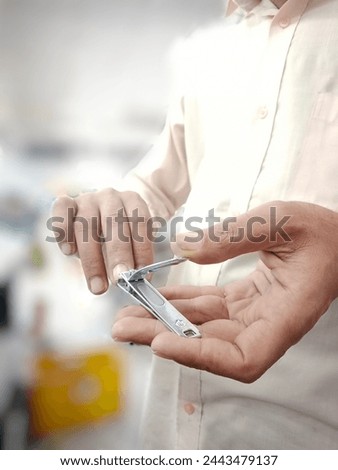 "Close-up of a man using a nail cutter to trim his nails, focusing on precision and personal grooming in a home setting." Royalty-Free Stock Photo #2443479137