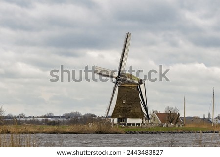 View of the historic thatched Veendermolen with miller's cottage on the bosom of the Weide Aa near the Dutch village of Roelofarendsveen against the background of a winter cloudy sky Royalty-Free Stock Photo #2443483827