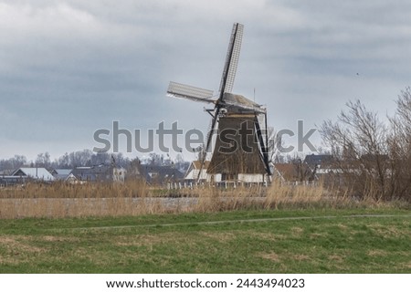 View of the historic thatched Veendermolen with miller's cottage on the bosom of the Weide Aa near the Dutch village of Roelofarendsveen against the background of a winter cloudy sky Royalty-Free Stock Photo #2443494023