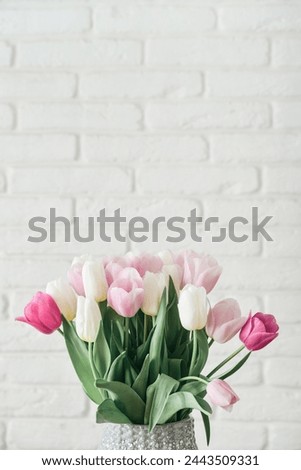 Bouquet of pink and white tulips in vase against white brick wall
